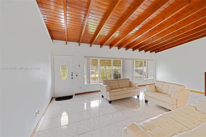 Vaulted ceiling with exposed wood beams, glossy tile flooring, and a glass-paneled entry door