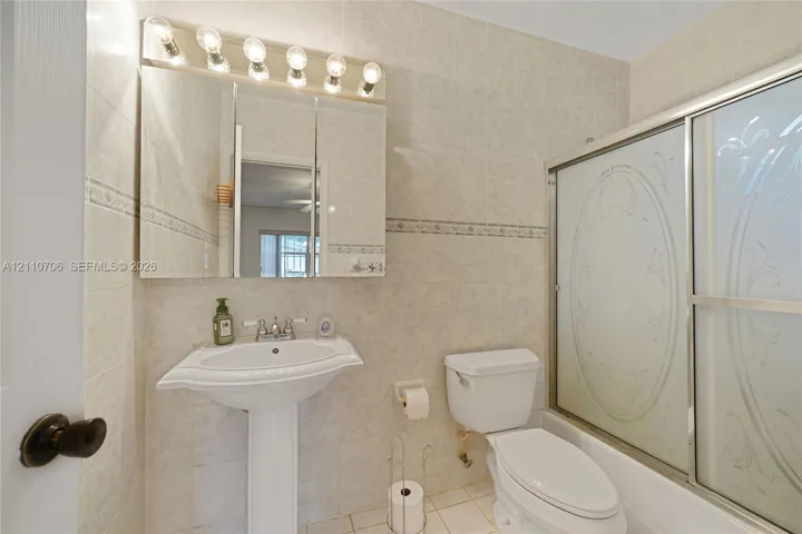 Pedestal sink with widespread faucet, mirrored medicine cabinet with integrated light fixture, full-height tile wall surround, and shower enclosure with etched glass sliding doors