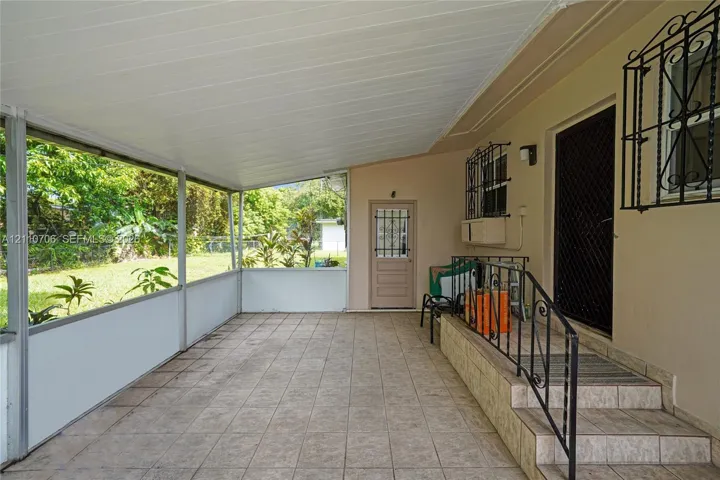 Screened-in porch featuring tiled flooring, a covered ceiling, ornamental wrought iron security bars on windows and doors, and a tiled staircase with a wrought iron railing