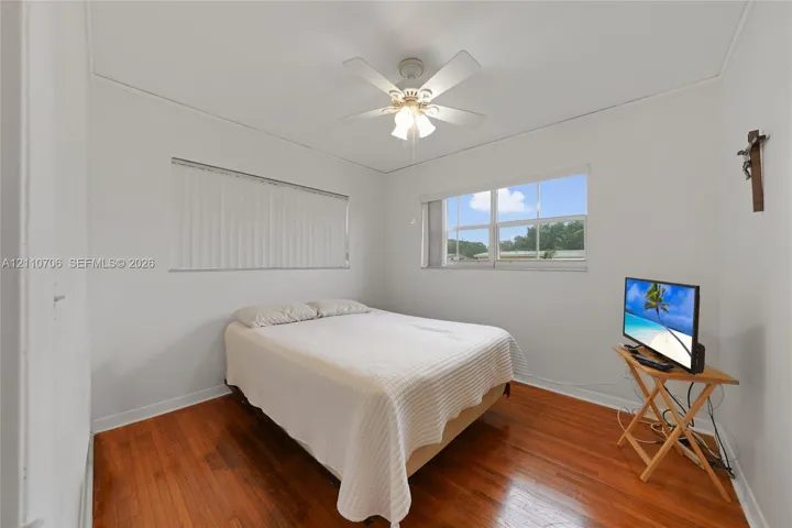 Interior room featuring wood-finish flooring, a white-bladed ceiling fan with a three-light fixture, and two windows with horizontal blinds