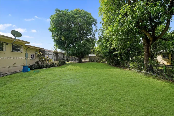 Expansive backyard featuring a large grass lawn, mature trees, and perimeter chain-link fencing