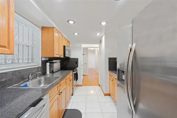 Kitchen featuring natural wood cabinetry, stone-finish countertops, stainless steel appliances, recessed lighting, and tile flooring