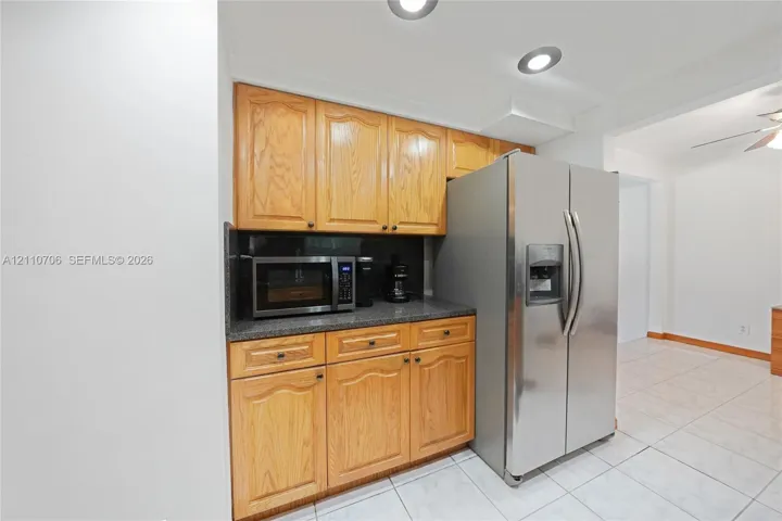 Kitchen featuring natural wood cabinetry, stone-finish countertops, stainless steel side-by-side refrigerator, and tile flooring with recessed lighting
