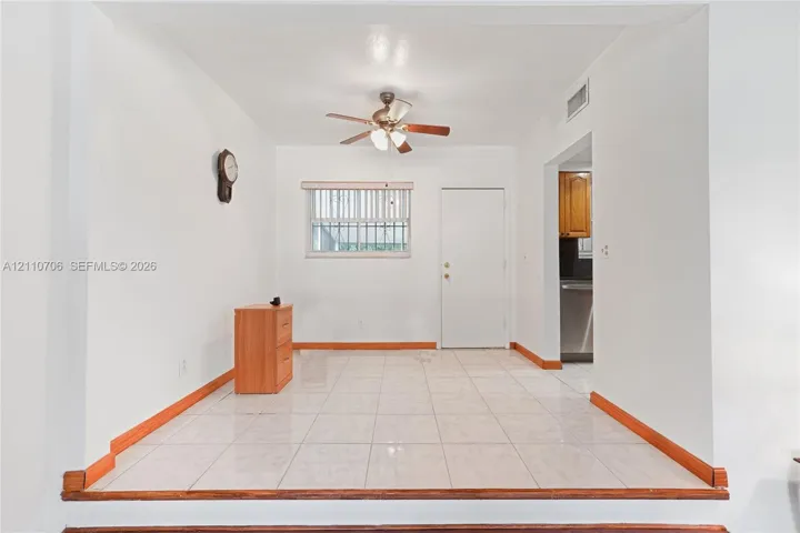 Raised floor area featuring large-format ceramic tile flooring, an elevated wooden threshold, a ceiling fan with integrated lighting, and a window with blinds