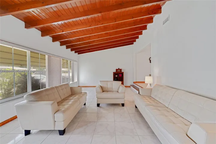 Vaulted ceiling featuring exposed wood beams, large windows, and tile flooring