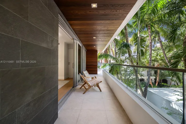 Covered balcony featuring large-format stone tile flooring, charcoal-toned stone wall cladding, natural wood-finish ceiling, and a glass panel railing