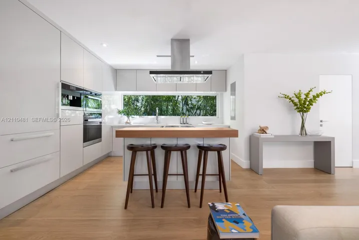 Contemporary kitchen featuring flat-panel cabinetry, stainless steel built-in ovens, wood-finish flooring, a center island with a wood countertop, and a stainless steel range hood