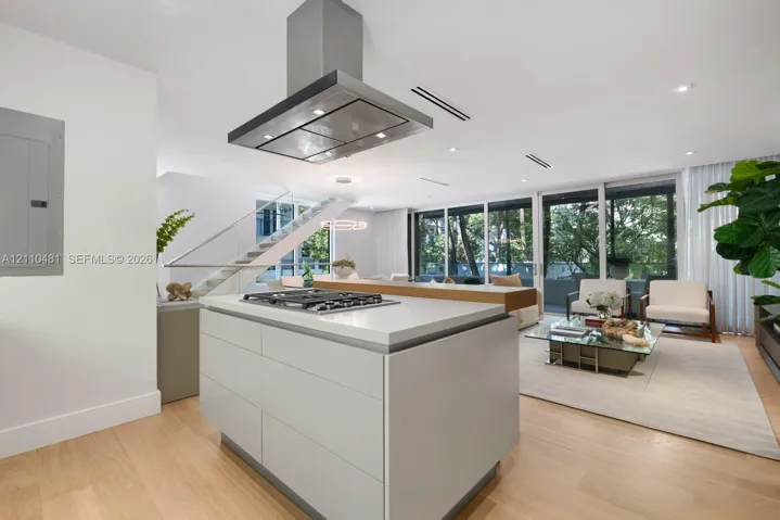 Kitchen island featuring a stone countertop, inset gas cooktop, and stainless steel hood range, complemented by wood-finish flooring and floor-to-ceiling windows