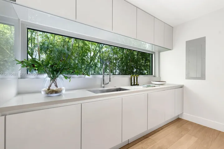 High-gloss white cabinetry, expansive horizontal picture window, solid-surface countertop, stainless steel pull-down faucet, and wood-finish flooring