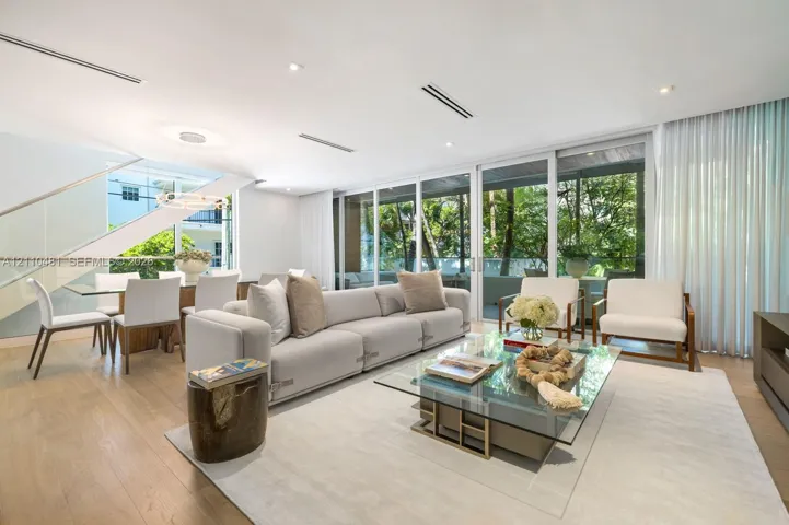 Open-concept living space featuring wood-finish flooring, floor-to-ceiling glass sliding doors, recessed ceiling lighting, and a floating staircase with a glass railing