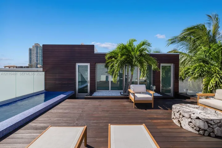 Rooftop terrace featuring dark wood decking, a built-in lap pool with mosaic tile surround, opaque glass railing, and wood-paneled exterior siding