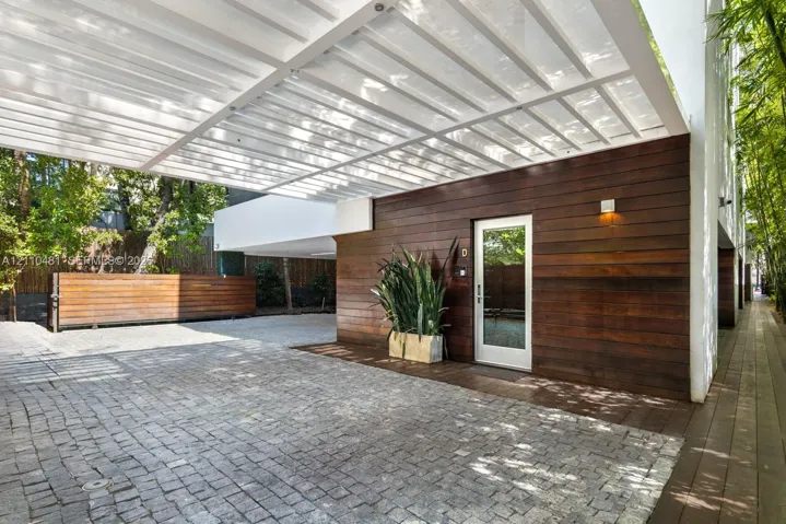 Modern exterior featuring horizontal wood siding, a structured metal pergola, stone paver driveway, and an entryway with a glass-paneled door