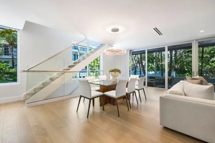Open-plan interior featuring light wood-finish flooring, floor-to-ceiling glass panels, and a staircase with glass railings and a wood handrail