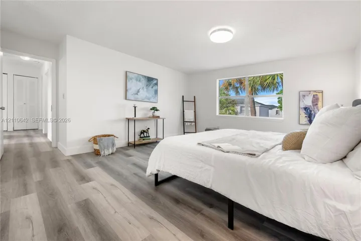 Neutral-toned wood-finish flooring, crisp white walls, dual-panel closet doors, and large single-hung window featuring outdoor palm tree greenery