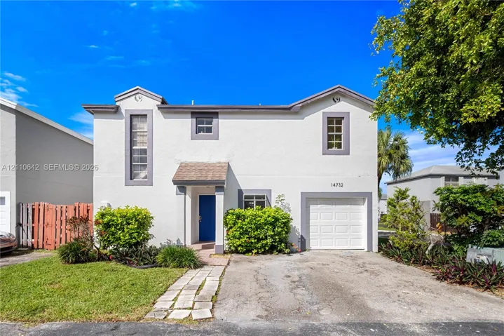 Two-story stucco exterior featuring a built-in single-car garage, defined entryway with a gabled porch cover, stone-paver walkway, and mature landscaping