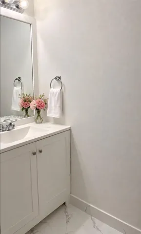 White vanity cabinet with a stone-composite countertop, integrated rectangular sink, chrome-finished faucet, framed mirror, and polished stone-finish floor tile