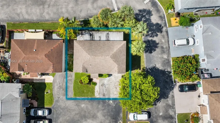 Aerial perspective featuring a hip-roof structure, concrete driveway, and landscaped front lawn with mature palms