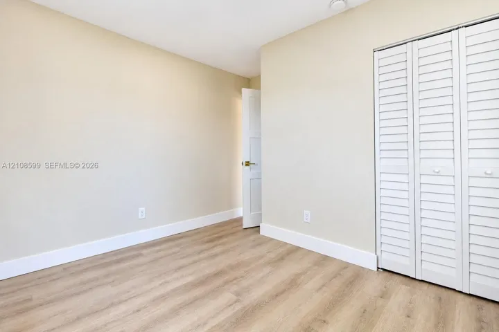 Interior room featuring wood-finish flooring, white louvered closet doors, and neutral wall paint