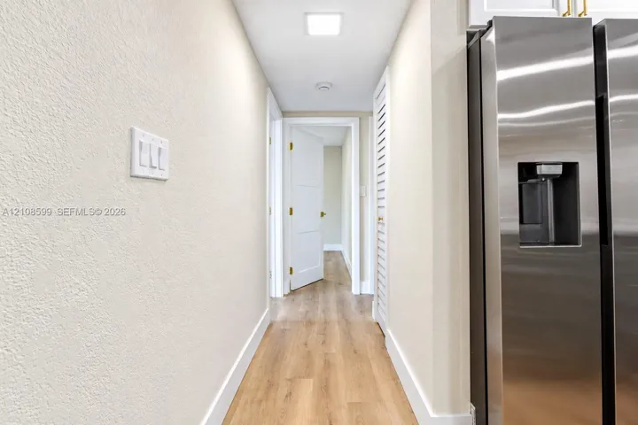 Stainless steel refrigerator, wood-finish flooring, white panel doors, and louvered closet doors