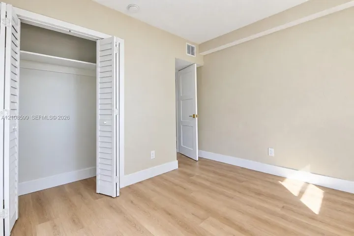 Interior space featuring wood-finish flooring, a closet with louvered bi-fold doors, and a paneled interior door with gold-tone hardware