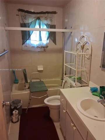 Full-height ceramic wall tiling, white bathtub with integrated shower, single-basin vanity with a solid-surface countertop, and polished chrome plumbing fixtures