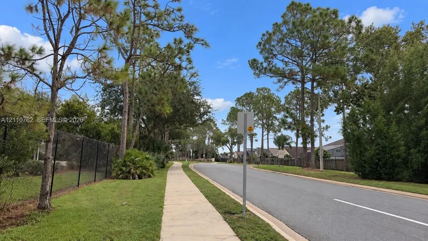 Paved concrete sidewalk bordering an asphalt street, characterized by mature trees and lush grassy areas