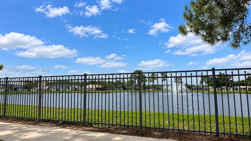 Waterfront lot featuring a metallic picket fence, maintained lawn, and a decorative fountain