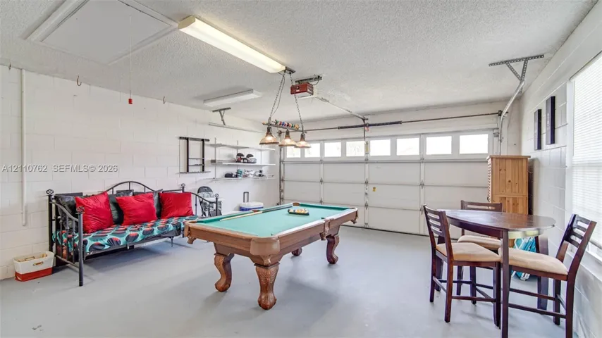 Multi-purpose garage space featuring painted masonry walls, a sectional overhead garage door, built-in wall shelving, and an industrial-style three-light pendant fixture