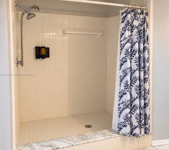 Walk-in shower featuring white wall tiling, a stone-finish threshold, and a wall-mounted metal shower head