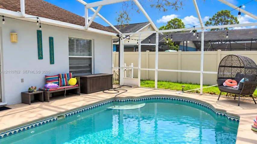 Screen-enclosed patio featuring a curved swimming pool, concrete deck, and vinyl perimeter fencing