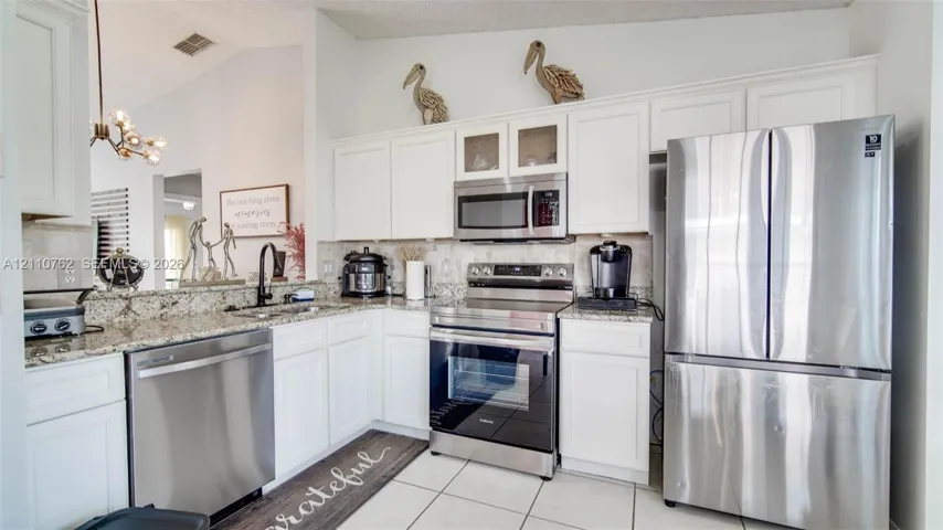 Kitchen featuring white shaker-style cabinetry, stone countertops, stainless steel appliances, a multi-light fixture, and ceramic tile flooring