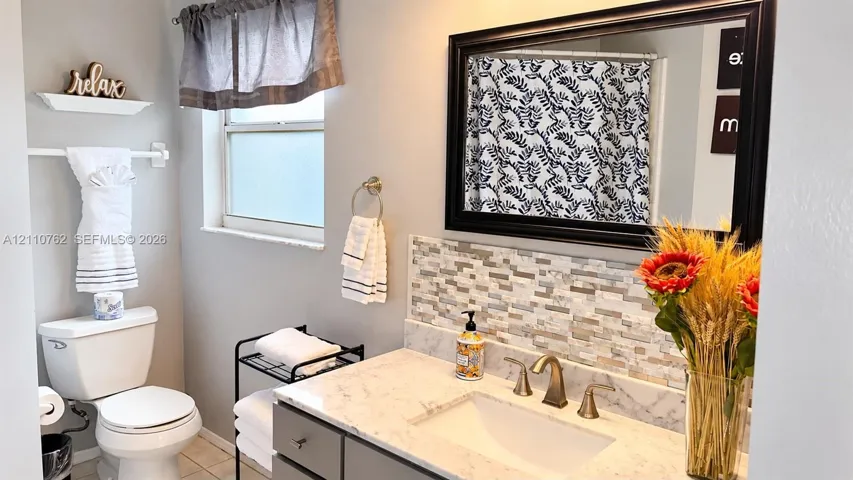 Vanity featuring a stone-look countertop, integrated rectangular sink, bronze-finish widespread faucet, and decorative stone-tile backsplash, paired with a framed wall mirror