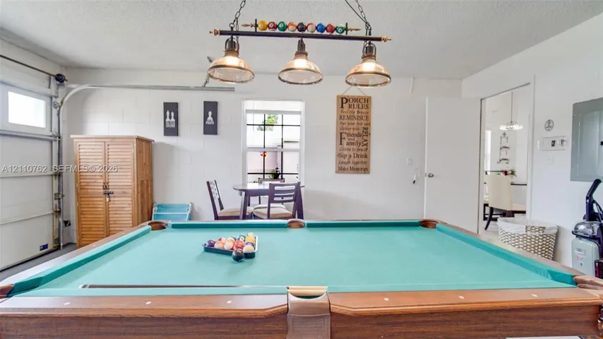 Multi-purpose space featuring a three-light metal billiard fixture, concrete block walls, and a single-pane window