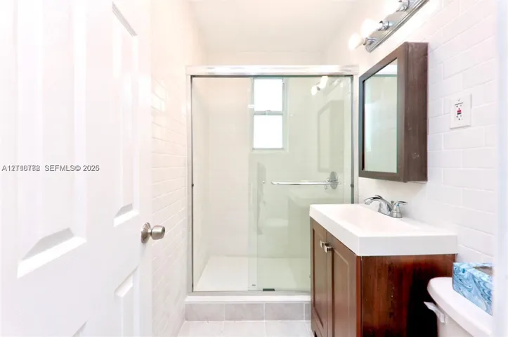 Walk-in glass-enclosed shower featuring white subway-style wall tile, dark wood-finish vanity with a rectangular sink, chrome fixtures, and a wall-mounted medicine cabinet