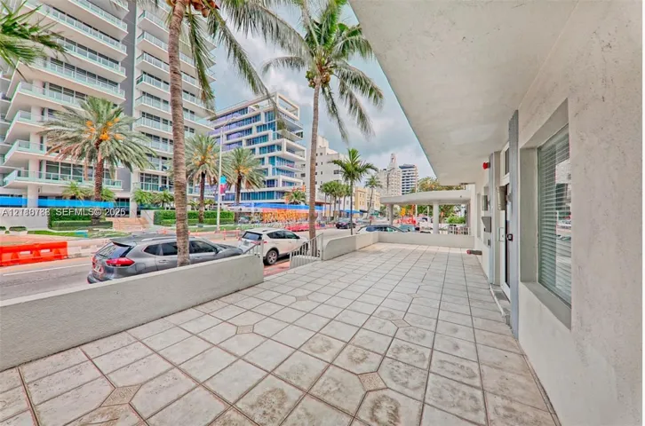 Covered exterior terrace featuring geometric tile flooring, concrete perimeter wall, and built-in glass paneled entry