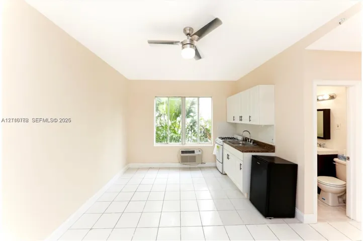 Kitchenette featuring white cabinetry, dark stone-finish countertops, stainless steel sink with pull-down faucet, and white ceramic tile flooring, complemented by a ceiling fan