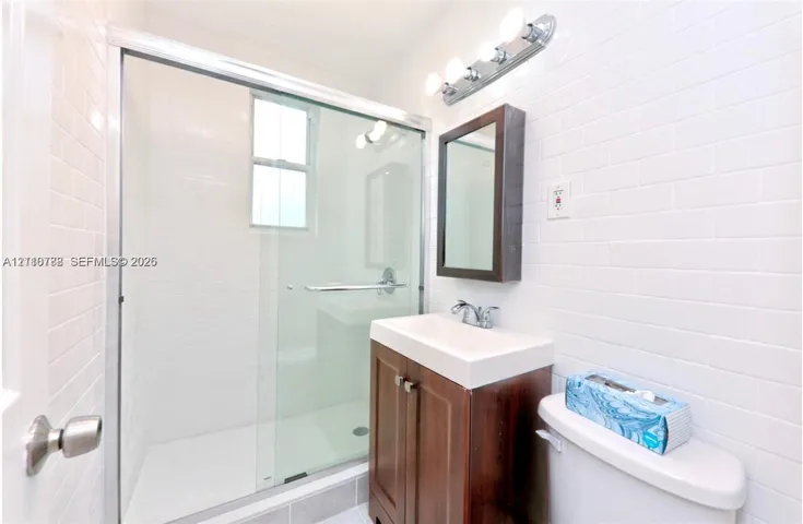 Bathroom featuring a glass-enclosed shower with subway tile surround, wood-finish vanity, rectangular wall-mounted medicine cabinet, and four-bulb vanity lighting