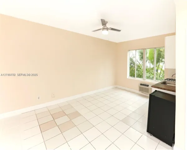 Interior space featuring neutral wall paint, white tile flooring, a ceiling fan with an integrated light fixture, large multi-pane windows, and a built-in kitchenette area with a sink