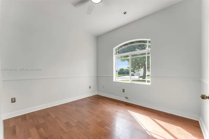 Room featuring wood-finish flooring, high ceilings, an arched window with muntins, and chair rail molding