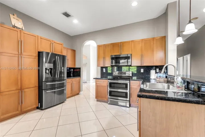 Kitchen featuring shaker-style cabinetry, stainless steel appliances, dark stone countertops, tile flooring, and pendant lighting