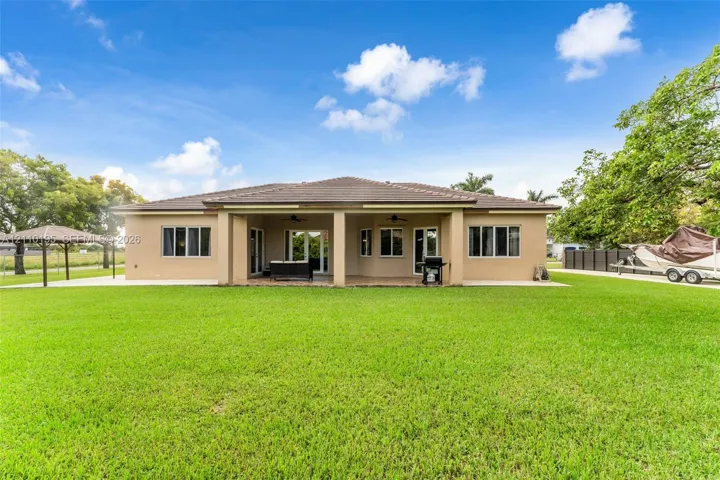 Spacious rear exterior featuring a covered patio, built-in ceiling fans, a detached gazebo, and expansive lawn
