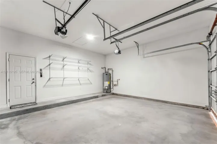 Attached garage featuring a concrete floor, finished interior walls, built-in wire wall shelving, and an automatic door opener