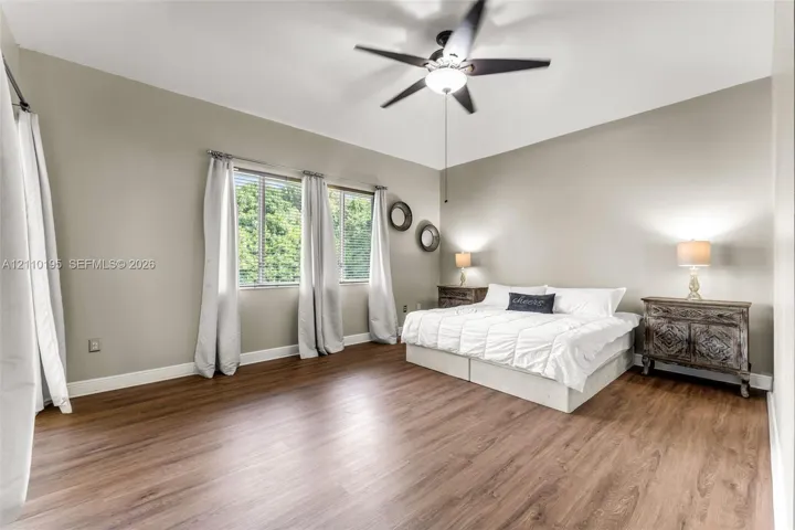 Neutral interior featuring wood-finish flooring, three windows with natural light, and a central ceiling fan