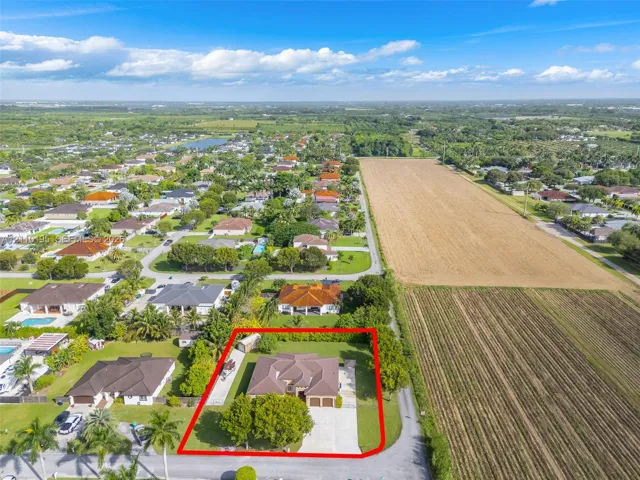 Aerial perspective of a detached residential property featuring a hipped roof, multi-car garage, concrete driveway, and mature landscaping within a bordered lot