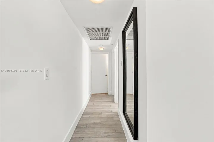 Hallway featuring wood-finish tile flooring, a recessed ceiling light, and a wall-mounted full-length mirror with a dark frame