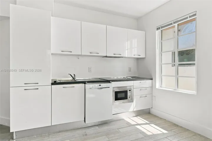 Kitchen featuring high-gloss white flat-panel cabinetry, dark countertop, integrated dishwasher, built-in microwave, and wood-finish flooring