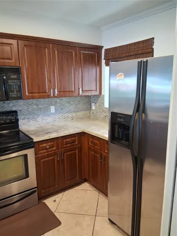 Kitchen featuring stained wood cabinetry, stone-finish countertops, geometric tile backsplash, and stainless steel appliances