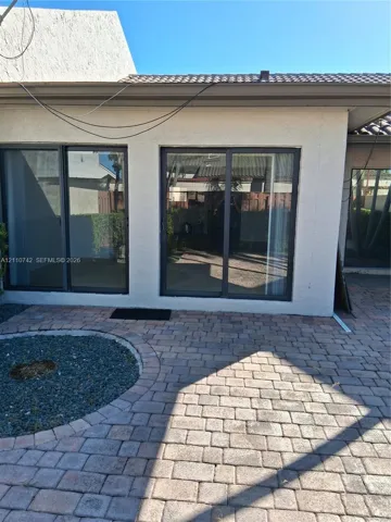 Stucco exterior featuring dual sliding glass doors, paver patio, and circular gravel garden bed