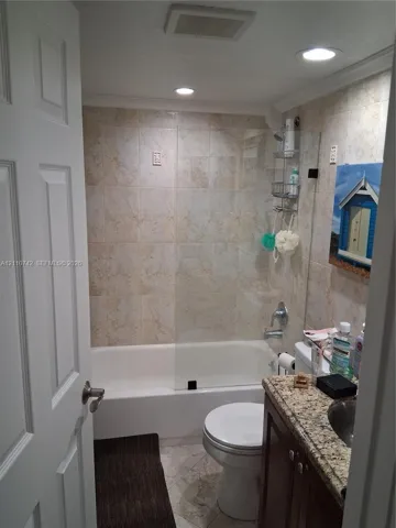 Full bathroom featuring a shower-tub combination with glass panel enclosure, tile-surround walls, stone-finish countertop, and recessed ceiling lighting