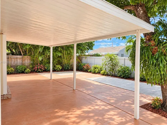 Covered patio featuring a stained concrete floor, metal support columns, wood-style ceiling paneling, perimeter fencing, and mature landscaping